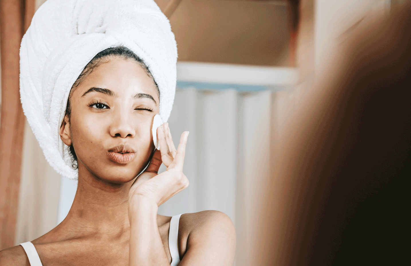 girl with head towel wiping her face with a cotton pad