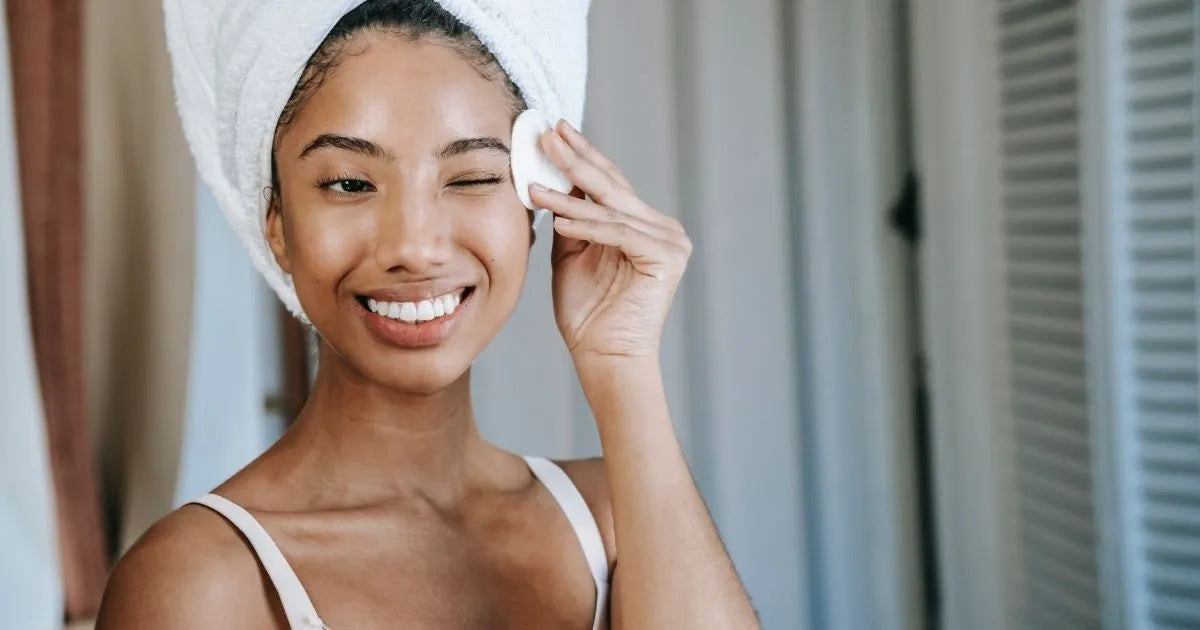 girl in a head towel wiping her face with a cotton pad