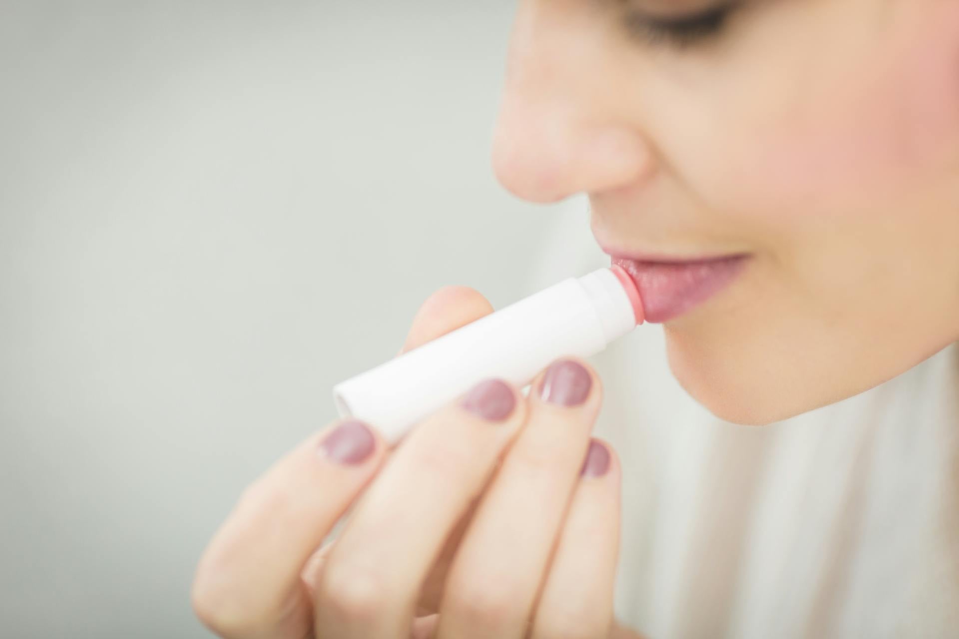 A woman swiping on a tinted lip butter on her lips.