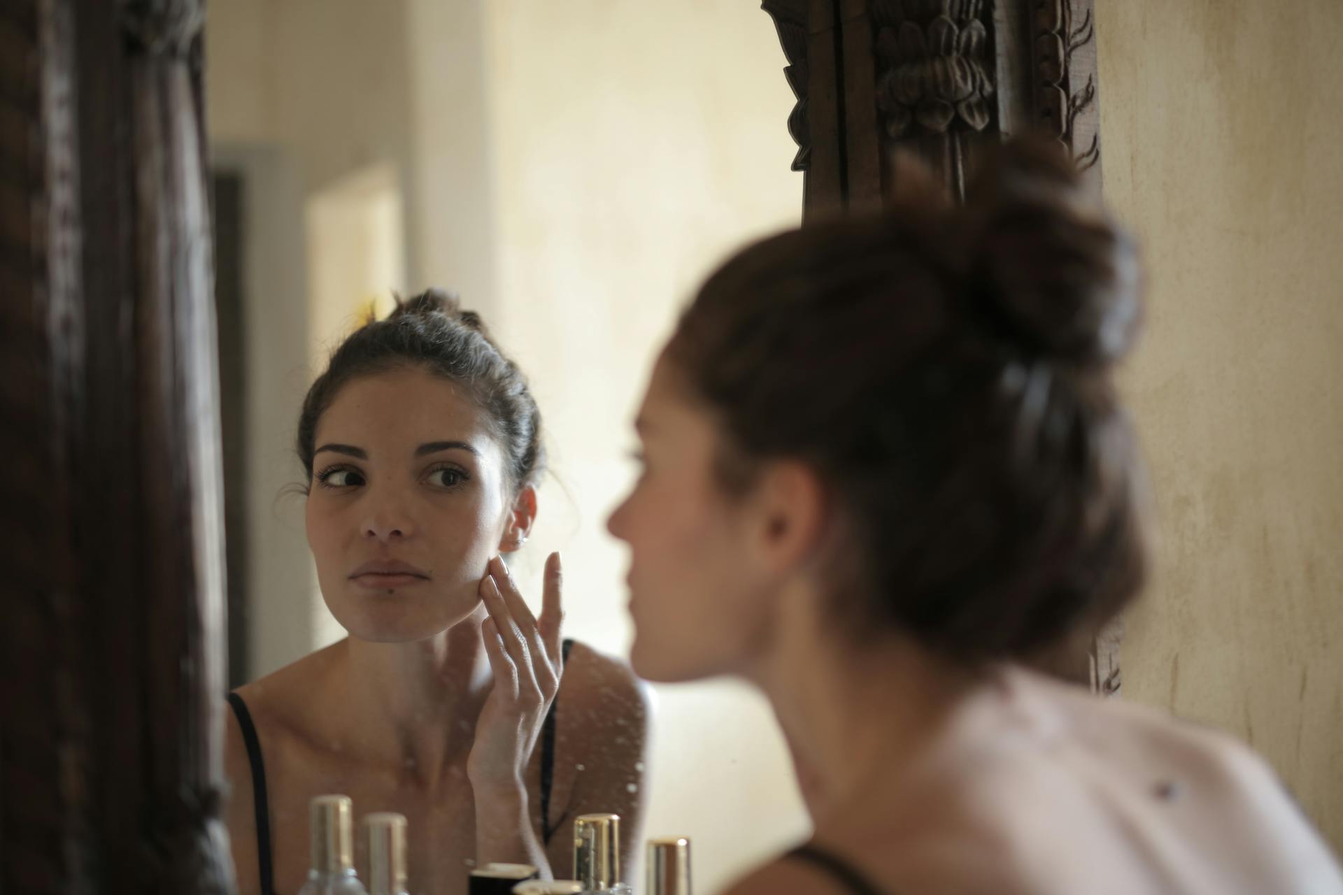 Woman applying toner on face while looking at the mirror