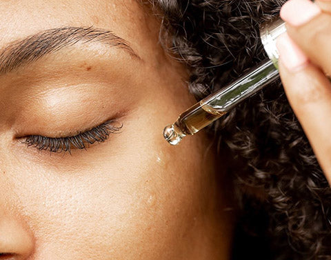 girl placing a drop of beauty oil on her cheek